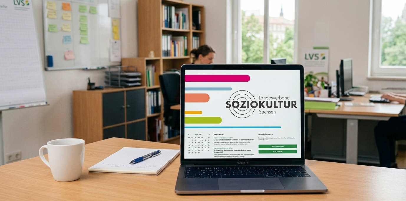 Laptop auf Schreibtisch im Büro, zeigt Website „Soziokultur Sachsen“, Personen arbeiten im Hintergrund