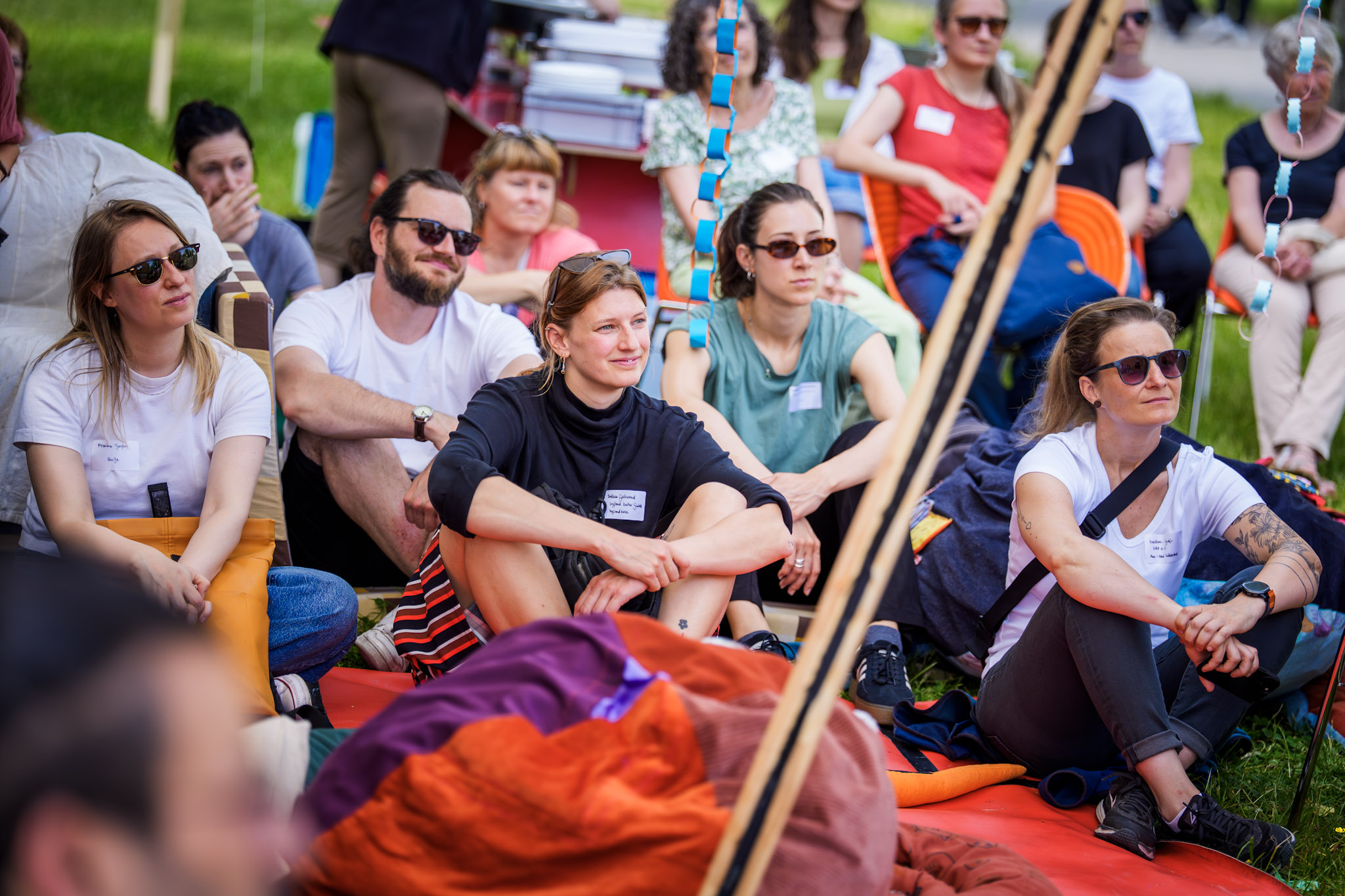 Eine Gruppe Menschen sitzt aufmerksam im Freien auf einer Wiese und hört einem Vortrag zu.