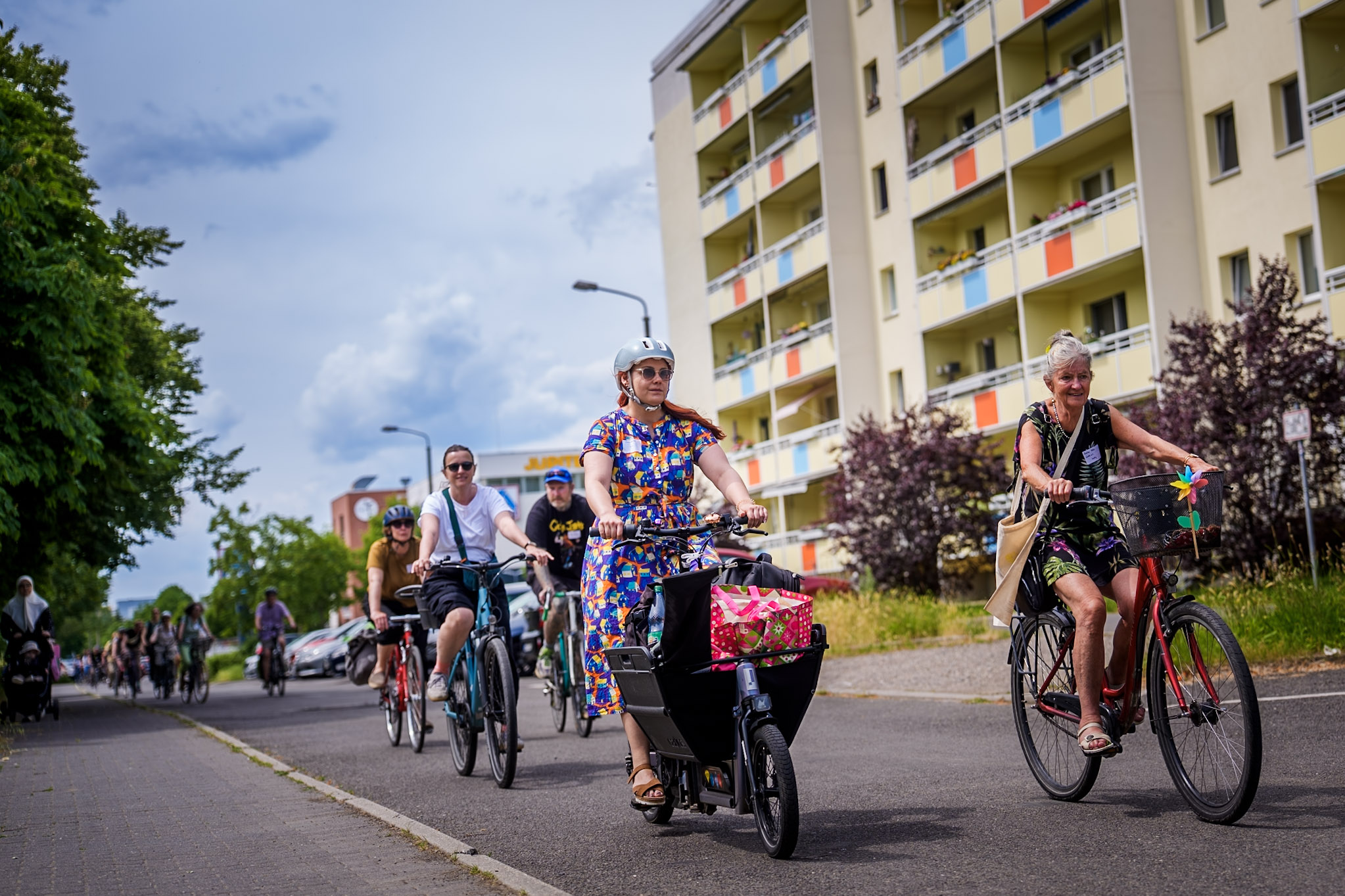 Gruppe von Radfahrenden fährt gemeinsam durch ein Wohnviertel mit Mehrfamilienhäusern.