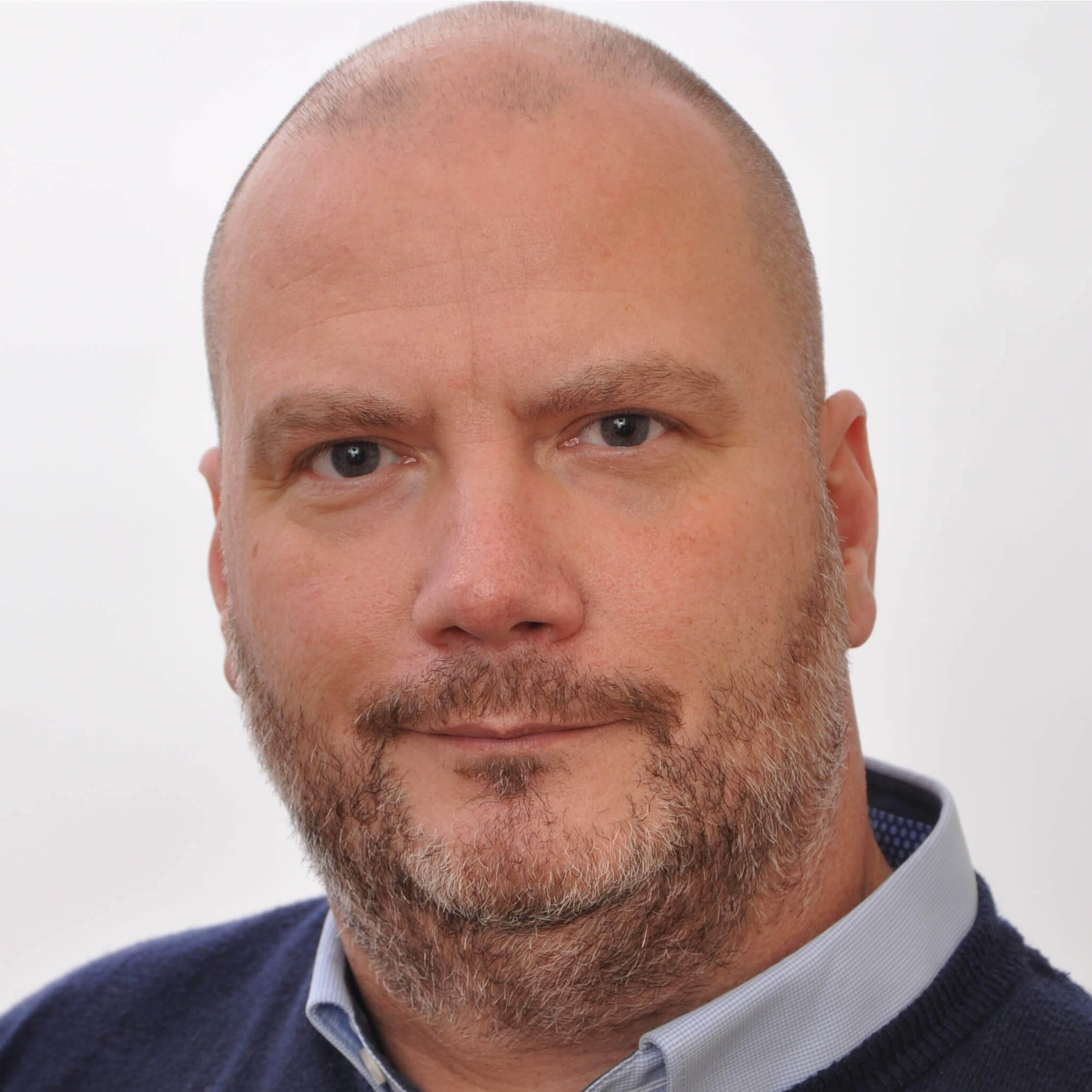 Ein lächelnder Mann mit kurzen, dunklen Haaren im dunkelblauen Hemd vor weißem Hintergrund.